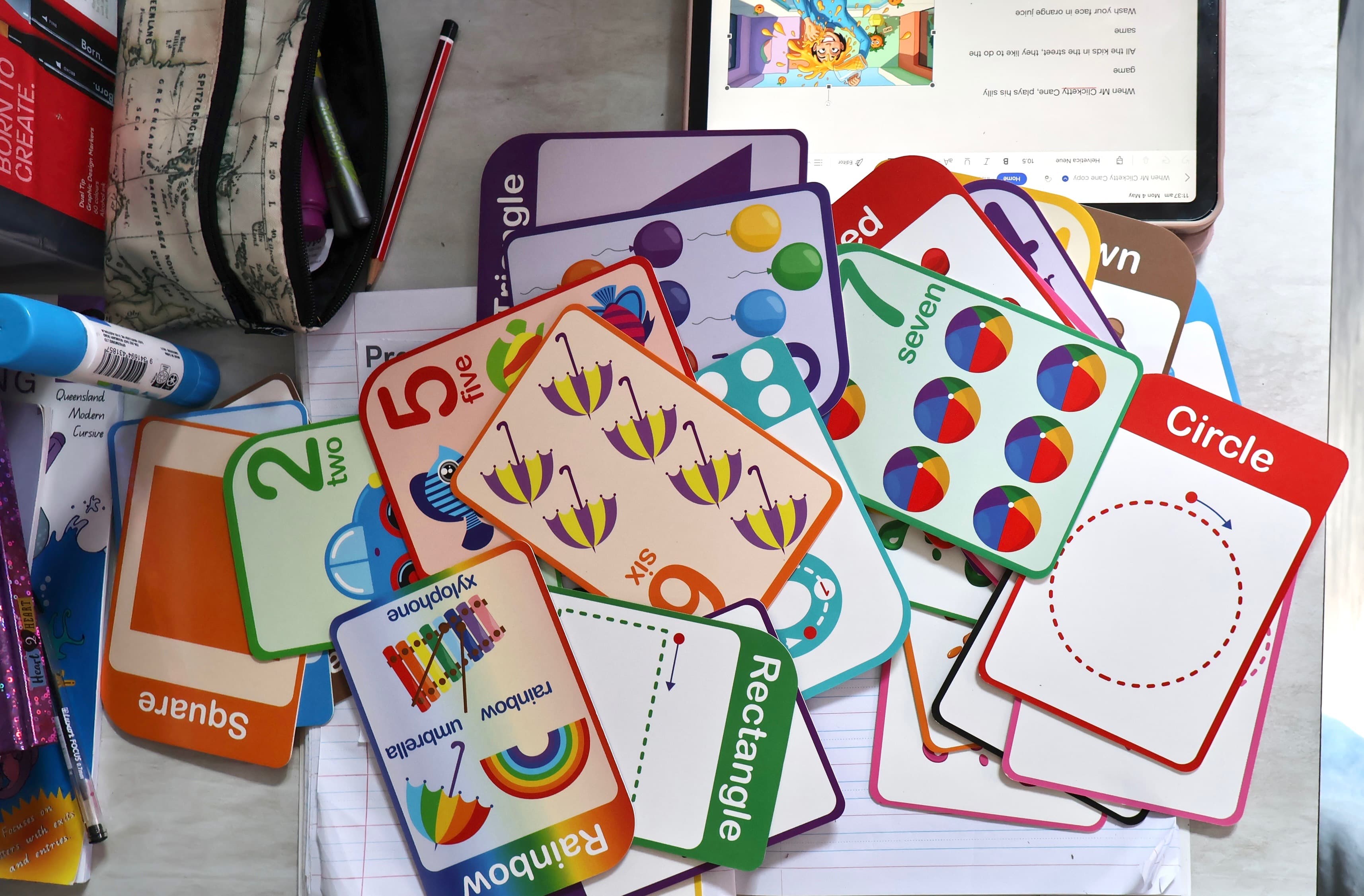 A desk covered in colourful primary-school flashcards, pencils and a notebook